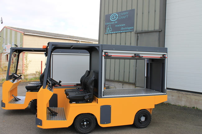 Deux véhicules utilitaires électriques jaunes Carry Craft à deux places, dont un avec compartiment latéral ouvert équipé d’un volet roulant.